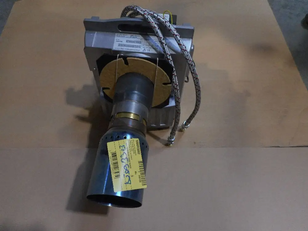 Ölbrenner von Remeha, sichtbar auf einem neutralen Untergrund, mit Metallanschlüssen und einem kurzen Auslassrohr. Einige technische Details sind auf einem Etikett angebracht.